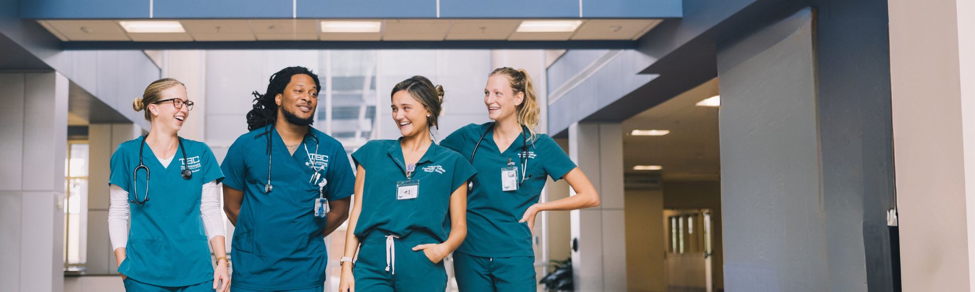 Four nursing students in scrubs smiling and laughing.