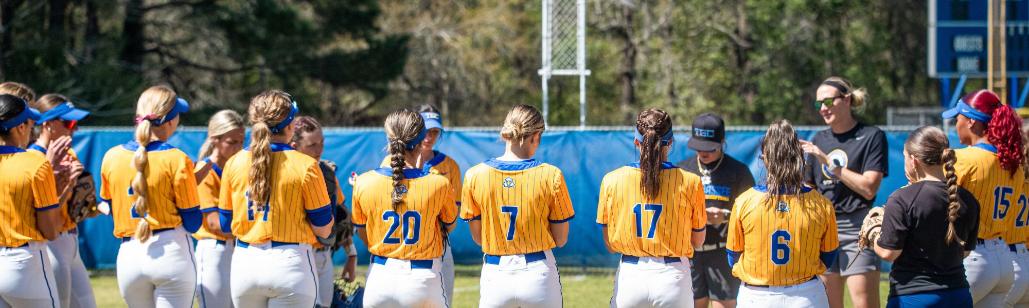 Softball team standing in a line and showing off their jersey numbers during practice.